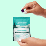 Hands holding a Green Roads Stress Aways Mixed Berry ashwagandha and CBD gummies pouch and a purple gummy.