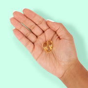Open hand holding three golden Green Roads CBD softgels against a mint background.
