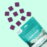Purple stress-away gummy candies scattered on a mint green background next to a teal and white 'Green Roads' pouch labeled 'Stress Away' and 'Zero THC'.