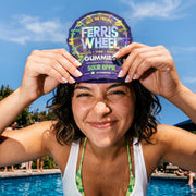 Person smiling by a pool, holding a Ferris Wheel Sour Apple 10-count gummies pouch above their forehead.