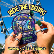 Hands holding a Ferris Wheel Sour Apple gummies pouch and a green gummy in front of a Ferris wheel.