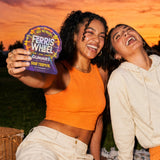 Two friends laughing outdoors at sunset, one holding a Ferris Wheel Sour Tropical 10-count gummies pouch.