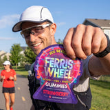 Runner smiling outdoors while holding a Ferris Wheel Strawberry 10-count gummies pouch toward the camera.