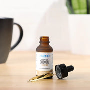 CBDMD 1500mg CBD Tincture bottle sitting on a wooden table, with a dropper filled with CBD oil positioned in front of it.