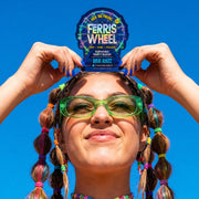 Person in green sunglasses holding a Ferris Wheel Blue Razz two-tablet pouch above their head against a blue sky.
