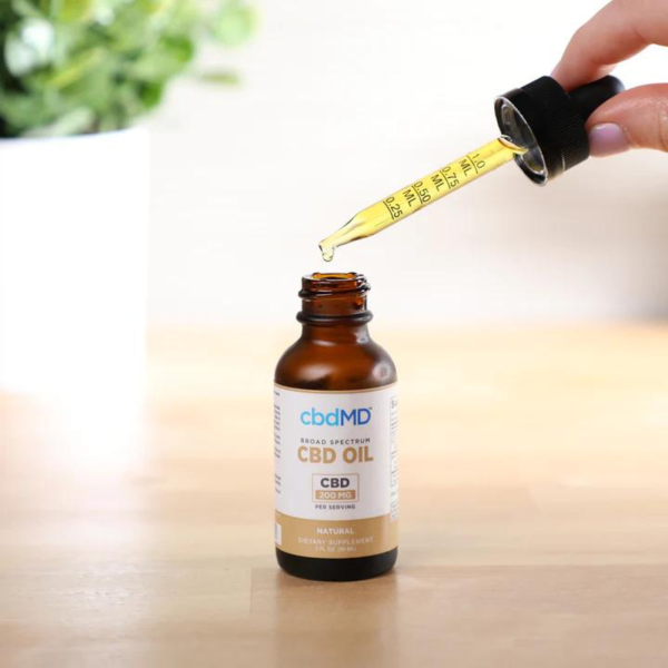 CBDMD 6000mg CBD Tincture bottle sitting on a wooden table, with a dropper filled with CBD oil positioned in front of it.