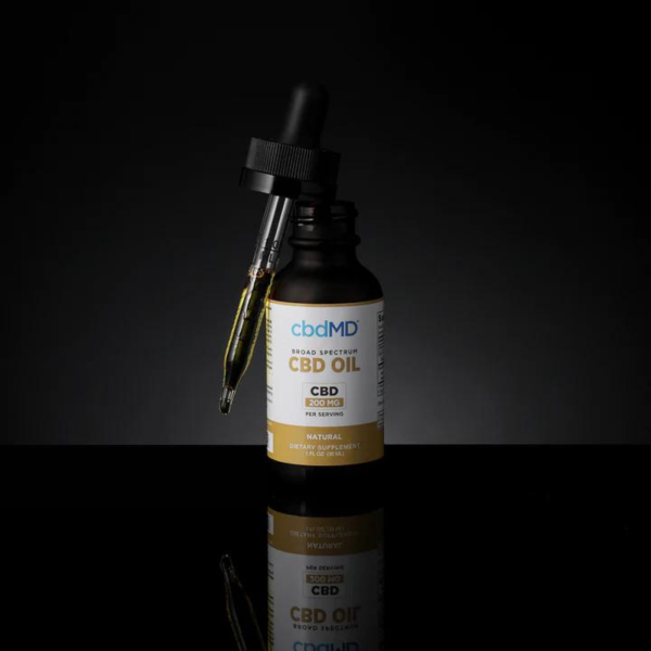 CBDMD 3000mg CBD Tincture bottle sitting on a glass table, with a dropper filled with CBD oil positioned in front of it.