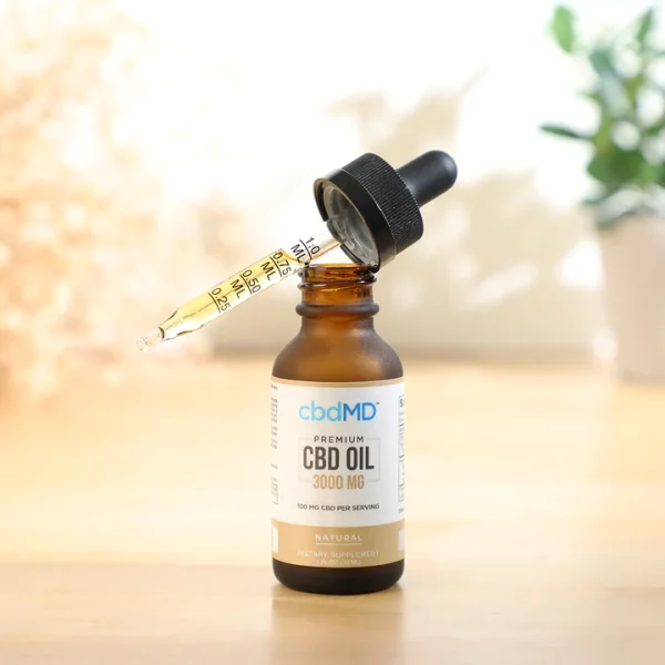 CBDMD 3000mg CBD Tincture bottle sitting on a wooden table, with a dropper filled with CBD oil positioned in front of it.