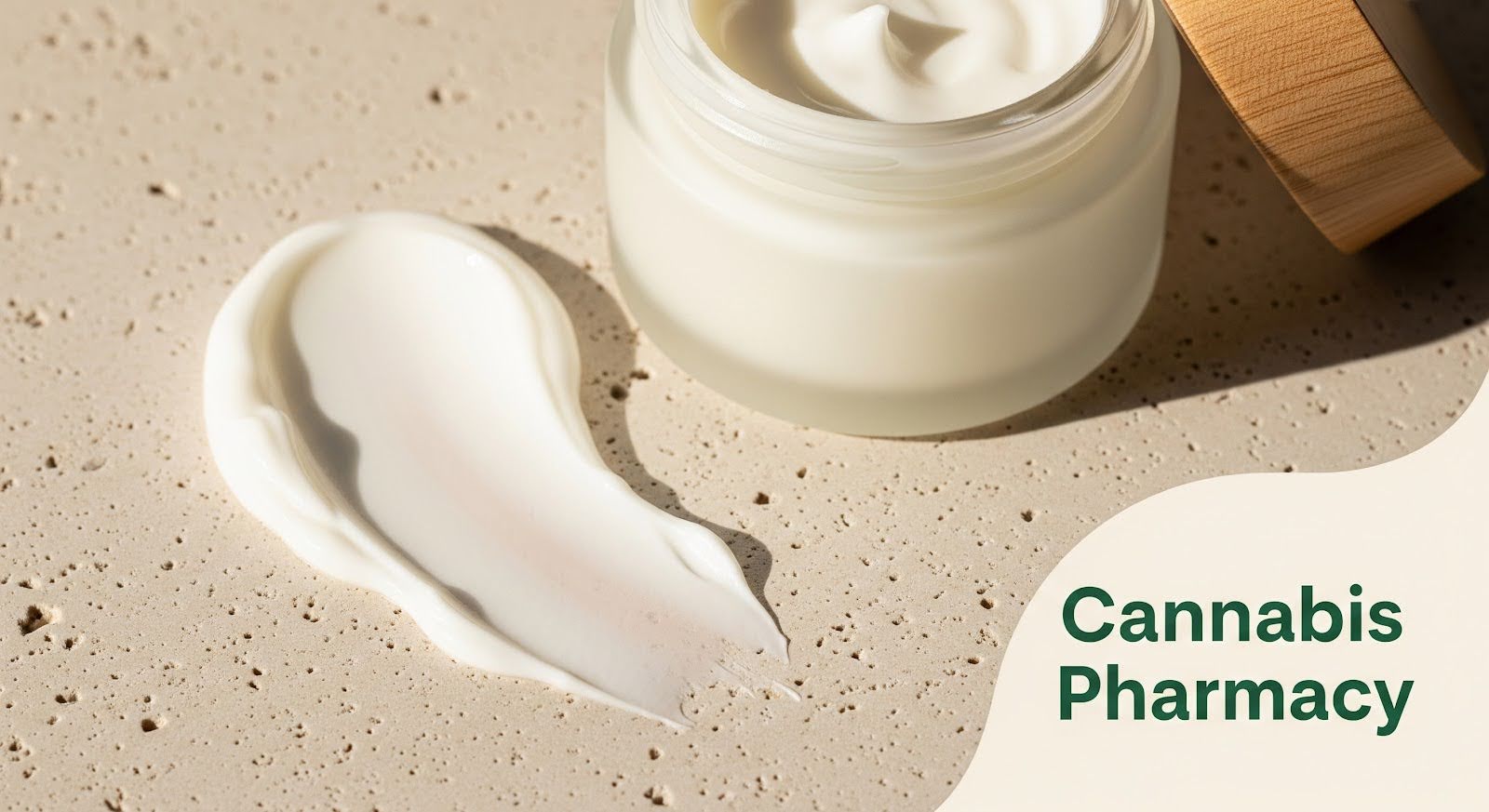 A jar of white cream with a wooden lid sits on a textured beige surface, with a smooth swipe of the cream spread beside it. The words "Cannabis Pharmacy" appear in green text on the lower right.